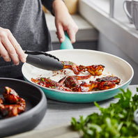 A person using tongs to pick up cooked bacon strips from the Rio Ceramic Nonstick 10" Frypan in the color Turquoise