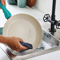 A person hand washing the Rio Ceramic Nonstick 10" Frypan in the color Turquoise in a kitchen sink