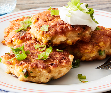 Plate of fried corn fritters topped with sour cream and green onions