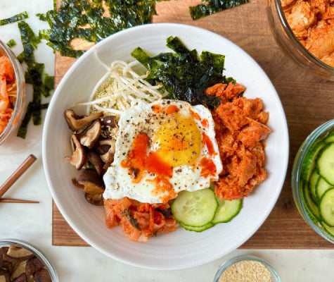 Colorful bowl of bibimbap - a bowl of rice topped with egg, kimchi, mushrooms, seaweed paper, bean sprouts, tinned fish, and more!