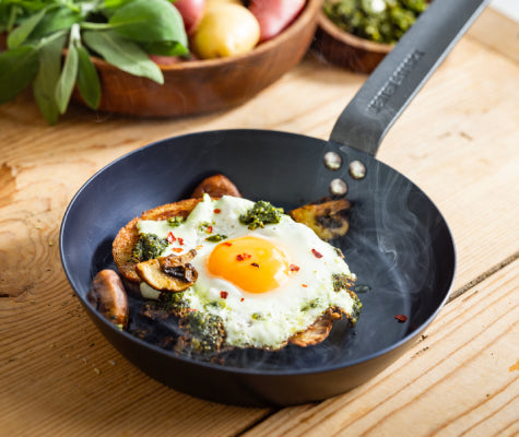 Merten and Storck 8-inch Carbon Steel Skillet on a wooden kitchen counter with a sunny-side up eggs and mushrooms steaming on the pan