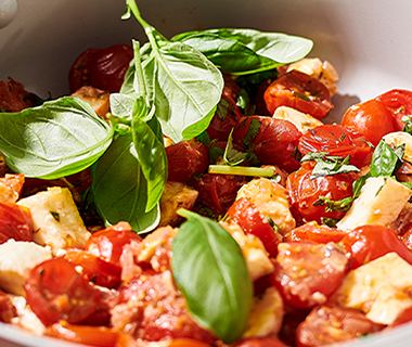 Sautéed cherry tomatoes, mozzarella cubes, and spinach leaves in a frypan