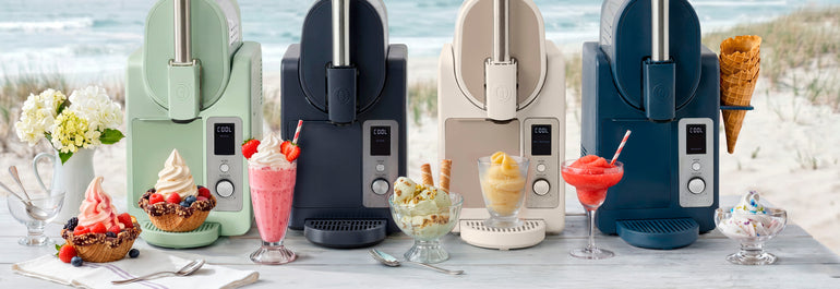 Four soft-serve ice cream machines in pastel colors on a beachside table, each with a dessert: sundae, milkshake, ice cream, and sorbet, with toppings and garnishes.