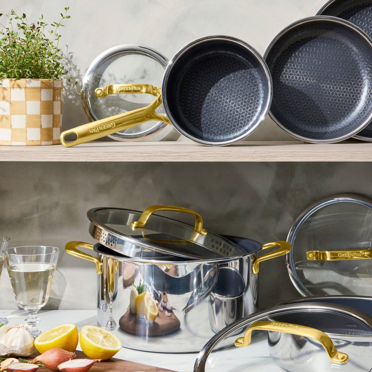 Gold ceramic nonstick cookware set with gold handles, surrounded by lemons and fresh herbs.