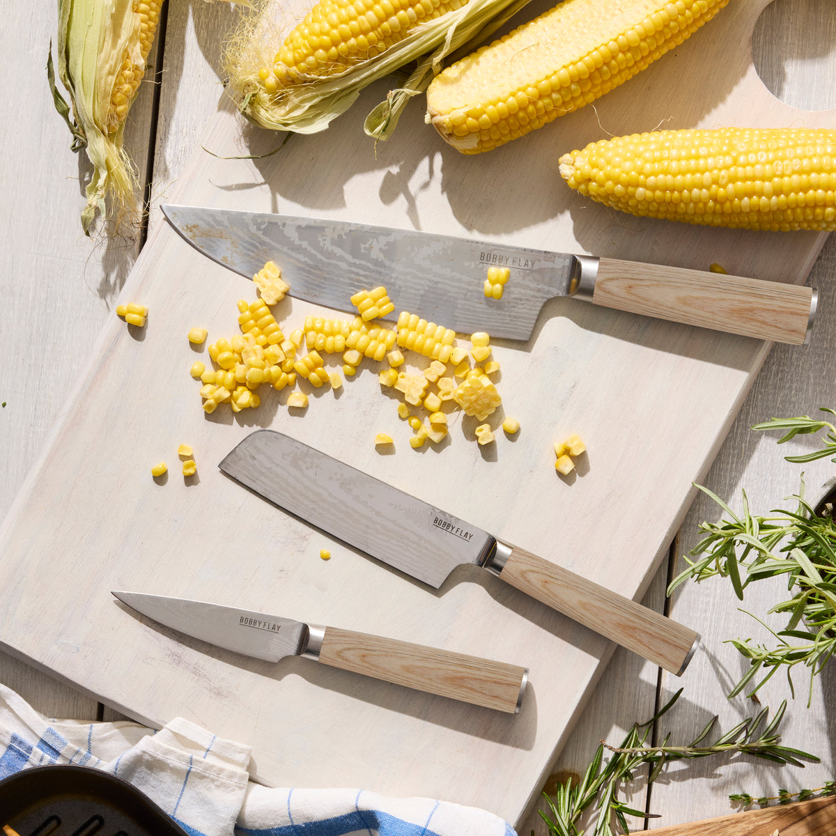 Knives on a cutting board with chopped corn and whole corn ears.