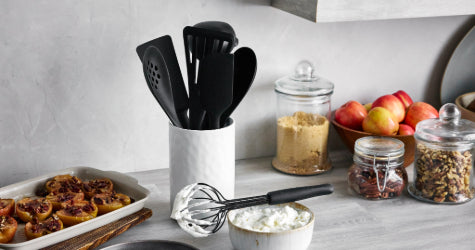 GreenPan skillet on a kitchen counter with utensil holder, jars of sugar and nuts, and a bowl of apples.