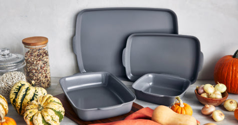 Set of three gray GreenPan ceramic baking dishes on a kitchen counter, with assorted squash, onions, pumpkin, and jars in the background.