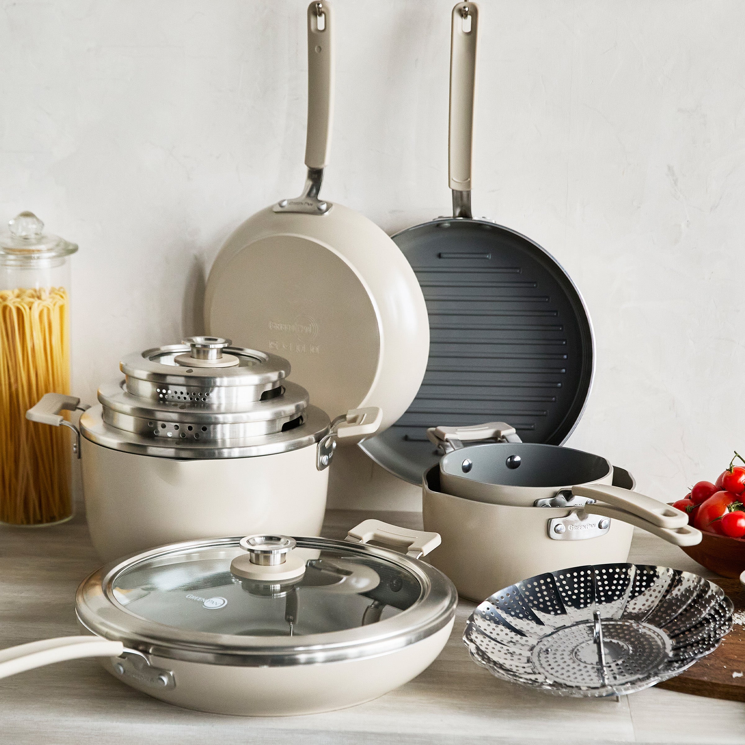 Set of cookware including pots, pans, and a grill pan on a light background