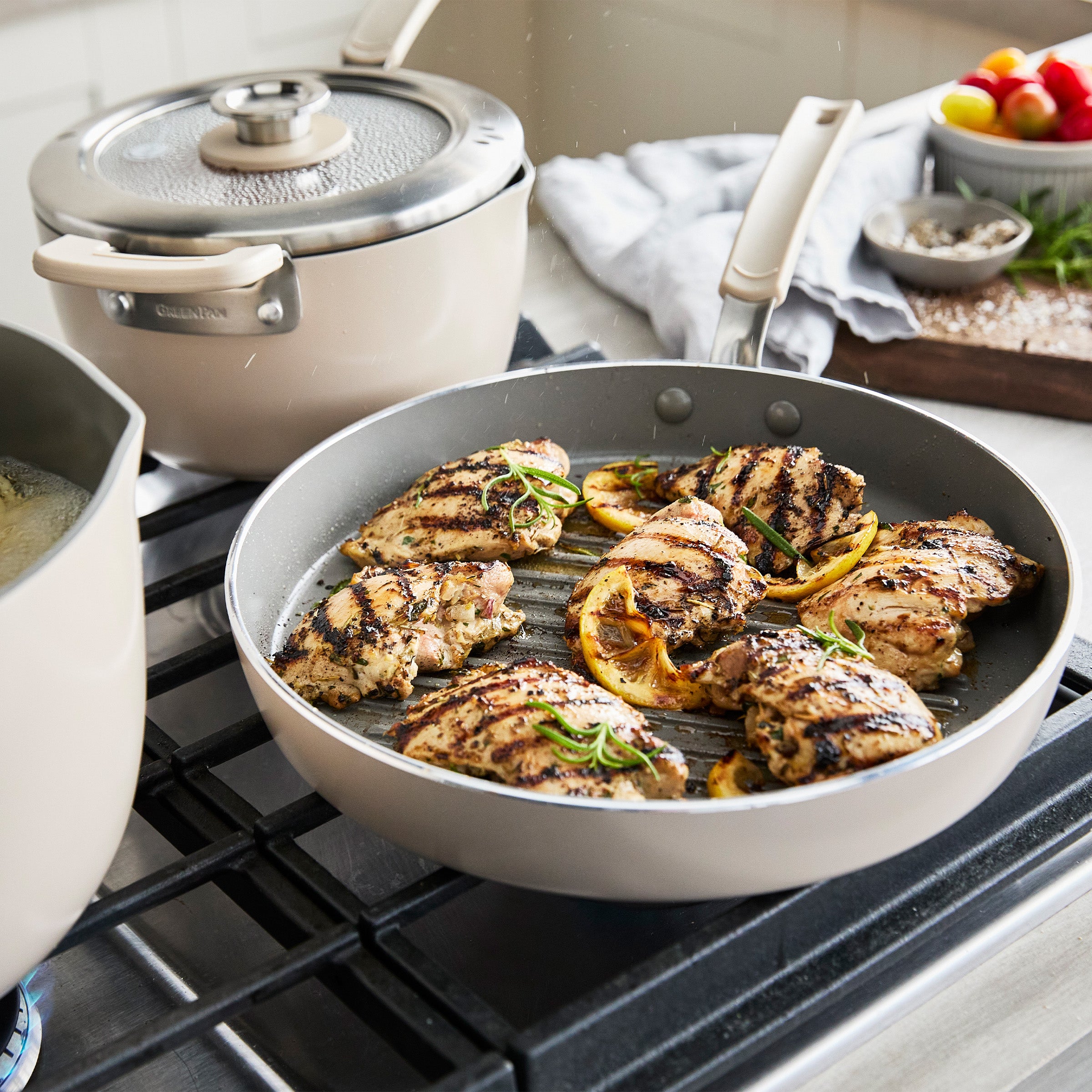 Cooked chicken with lemon and herbs in a frypan on a stove, with kitchenware and ingredients in the background