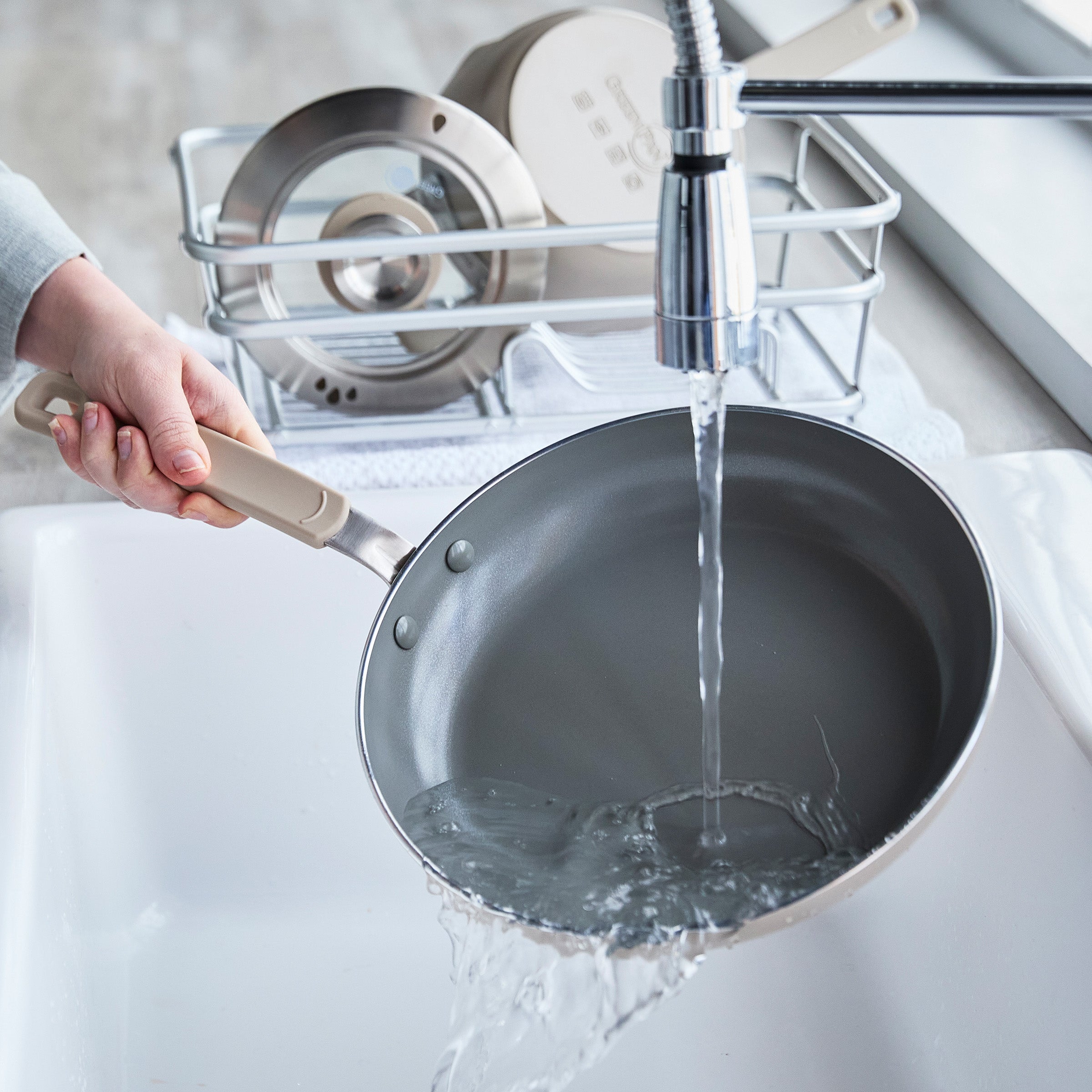 Person washing a frying pan under running water in a kitchen sink