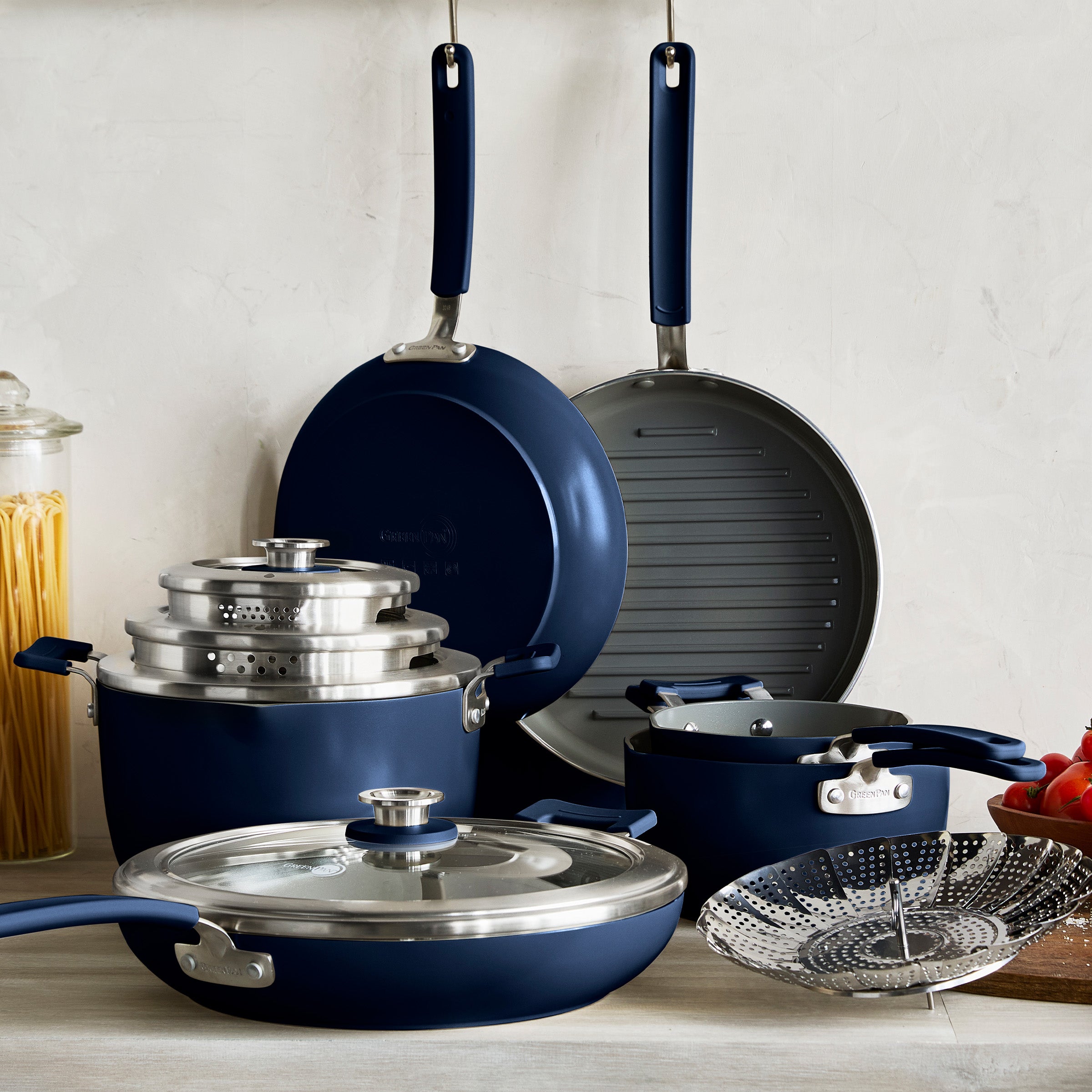 Set of cookware including pots, pans, and a grill pan on a light background