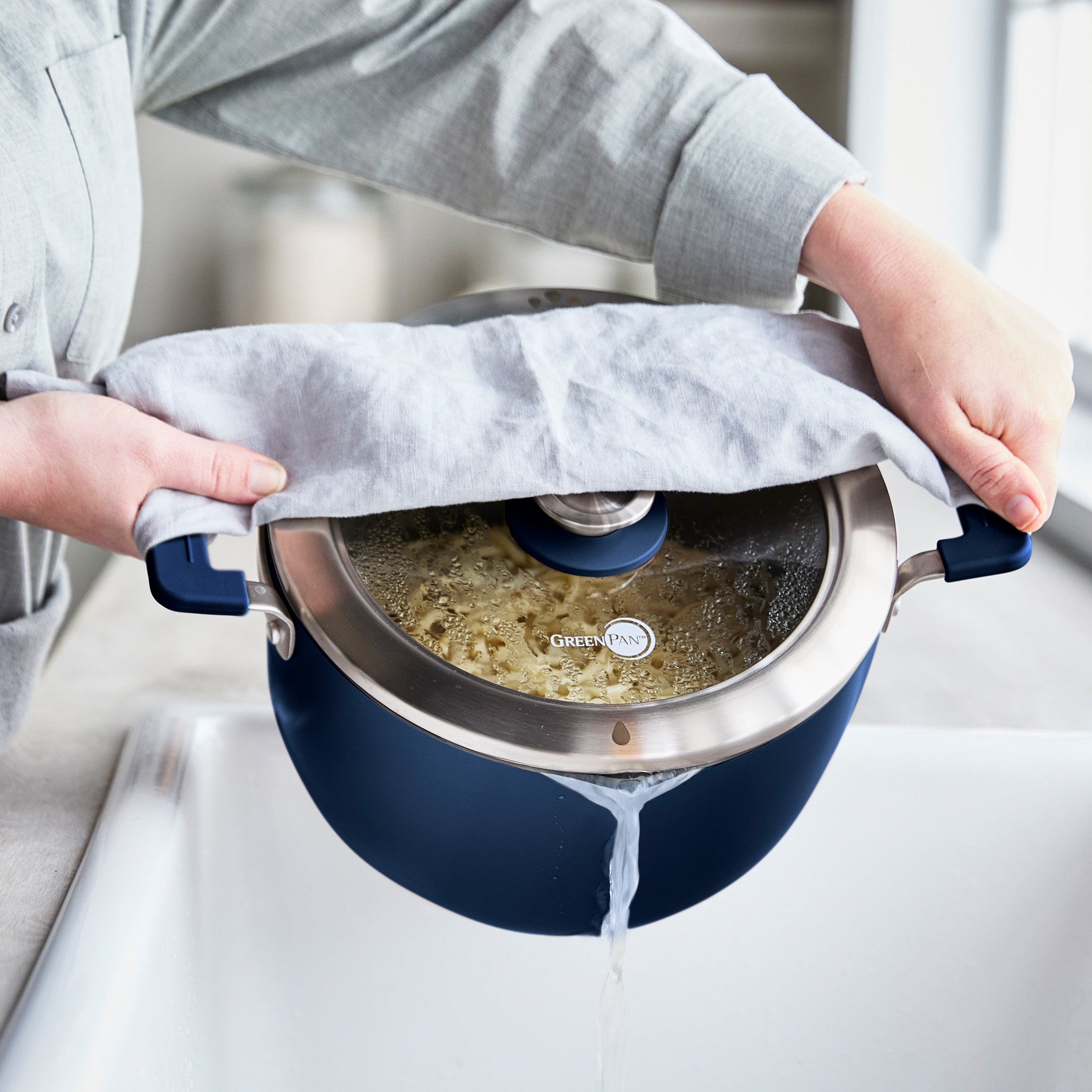 Person straining water from a stockpot into a kitchen sink