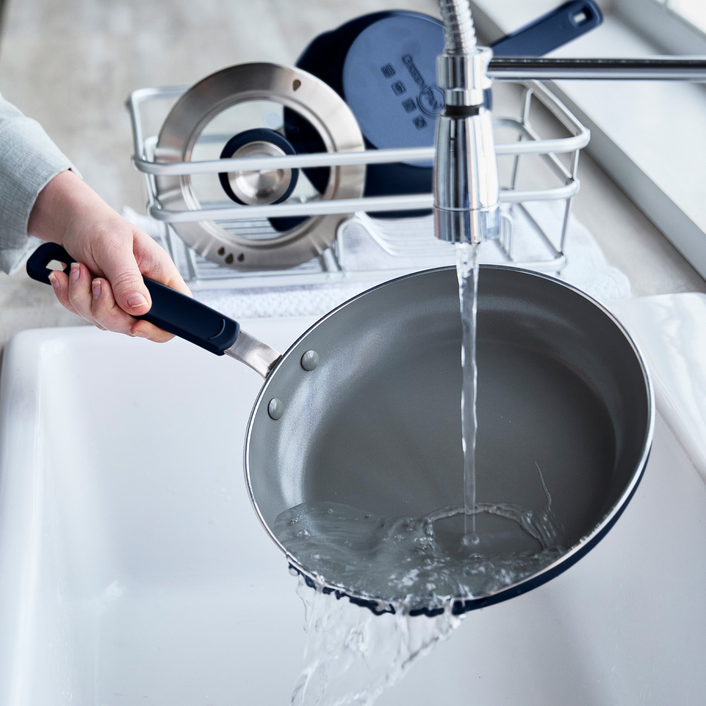 Person washing a frying pan under running water in a kitchen sink