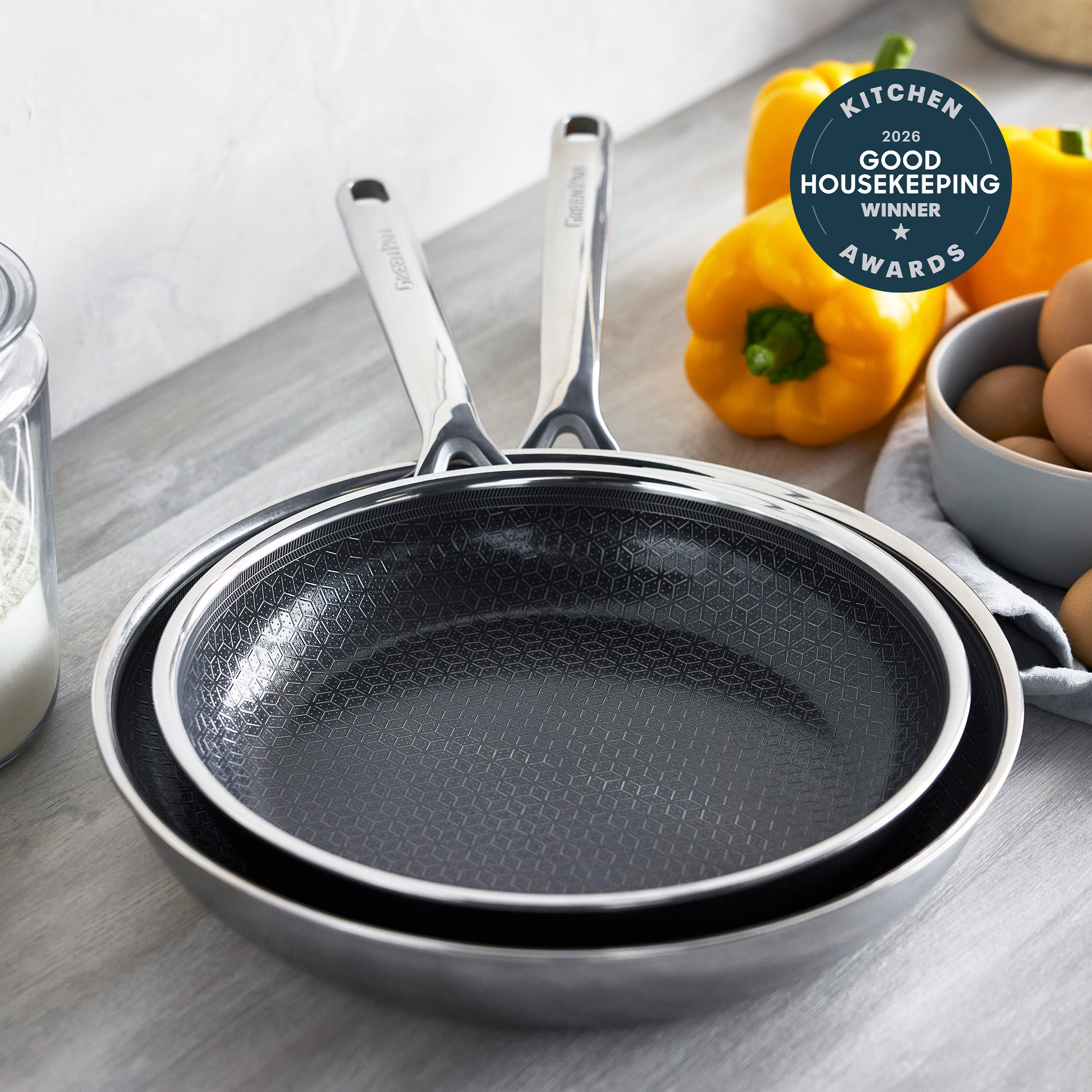 Two gray ceramic nonstick frypans, 10″ and 12″, on a counter with eggs, yellow peppers, and a GH award badge nearby.