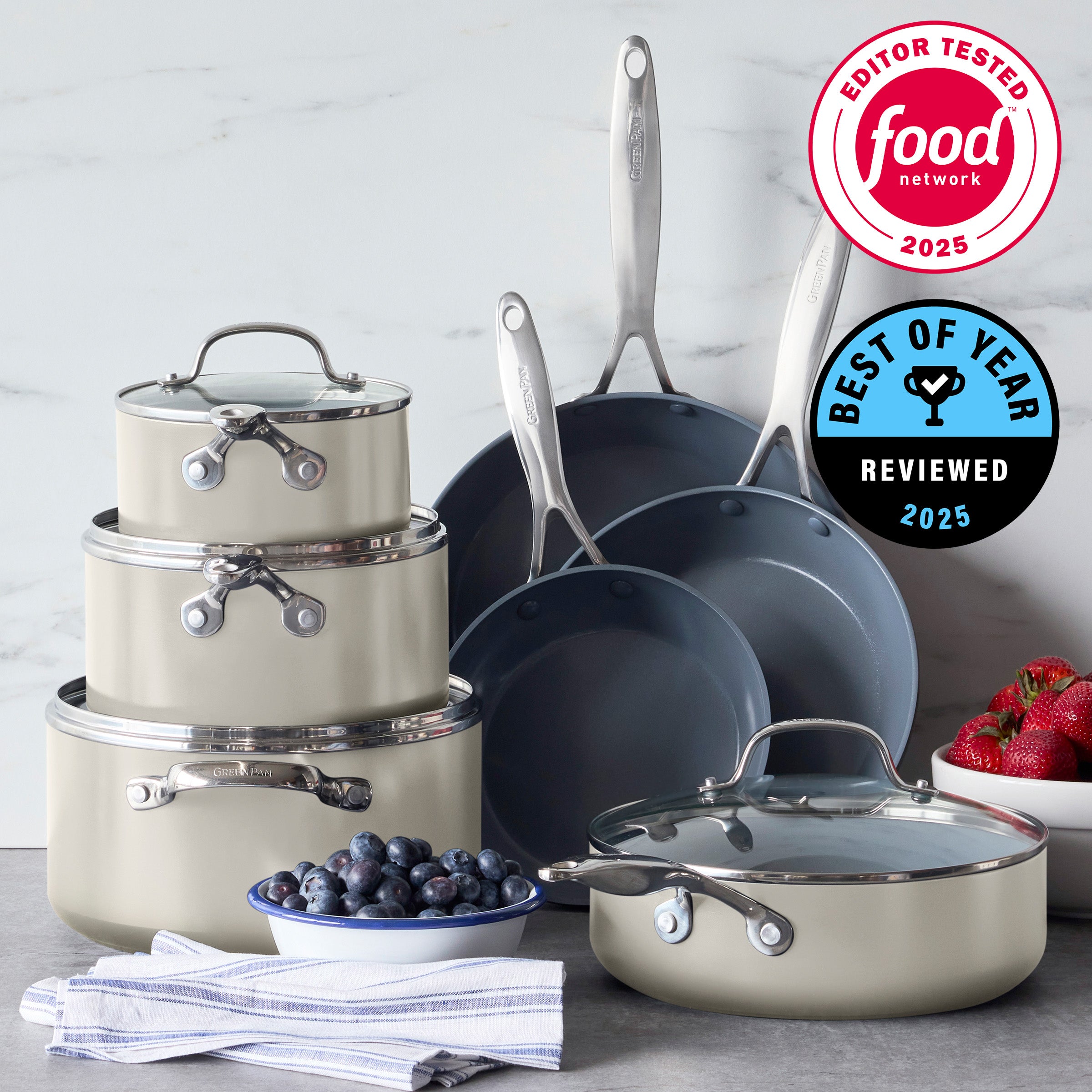 Cream ceramic nonstick 11-piece cookware set on a kitchen counter with berries and award plaques nearby.