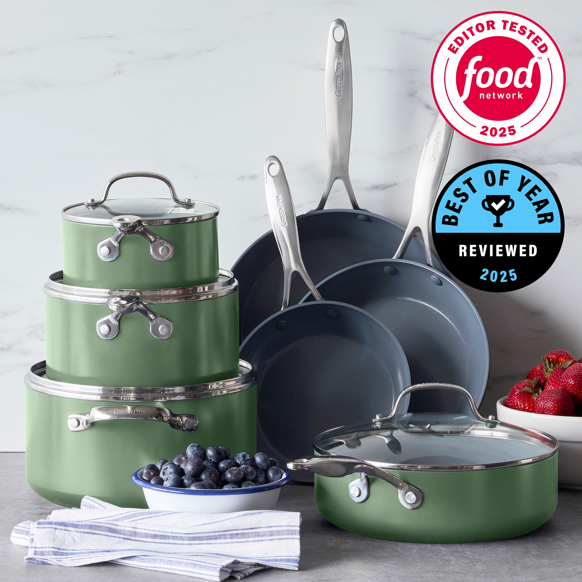 Sage green ceramic 11-piece cookware set with glass lids on counter, award badges above, berries nearby.