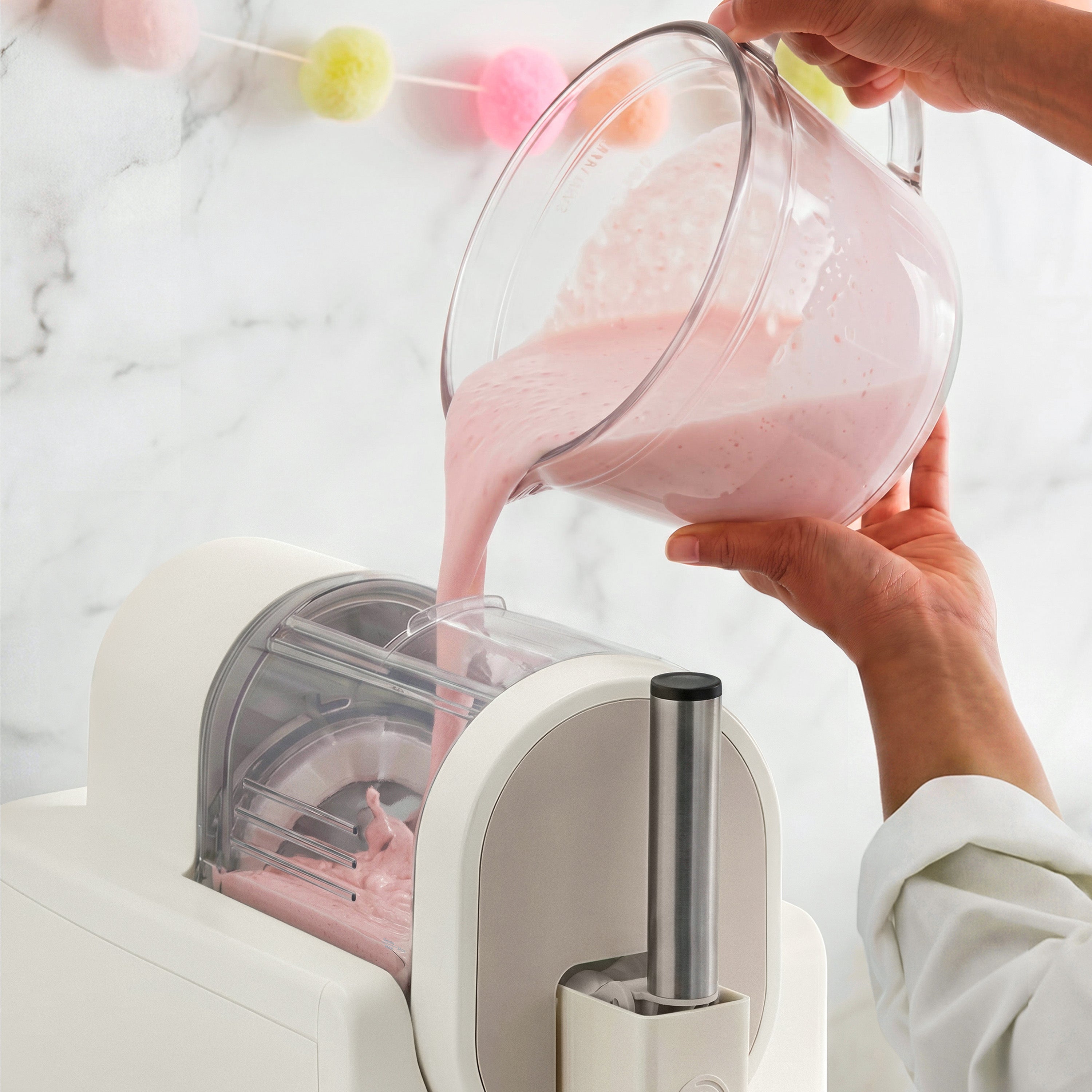 Person pouring pink liquid from a glass pitcher into an ice cream maker