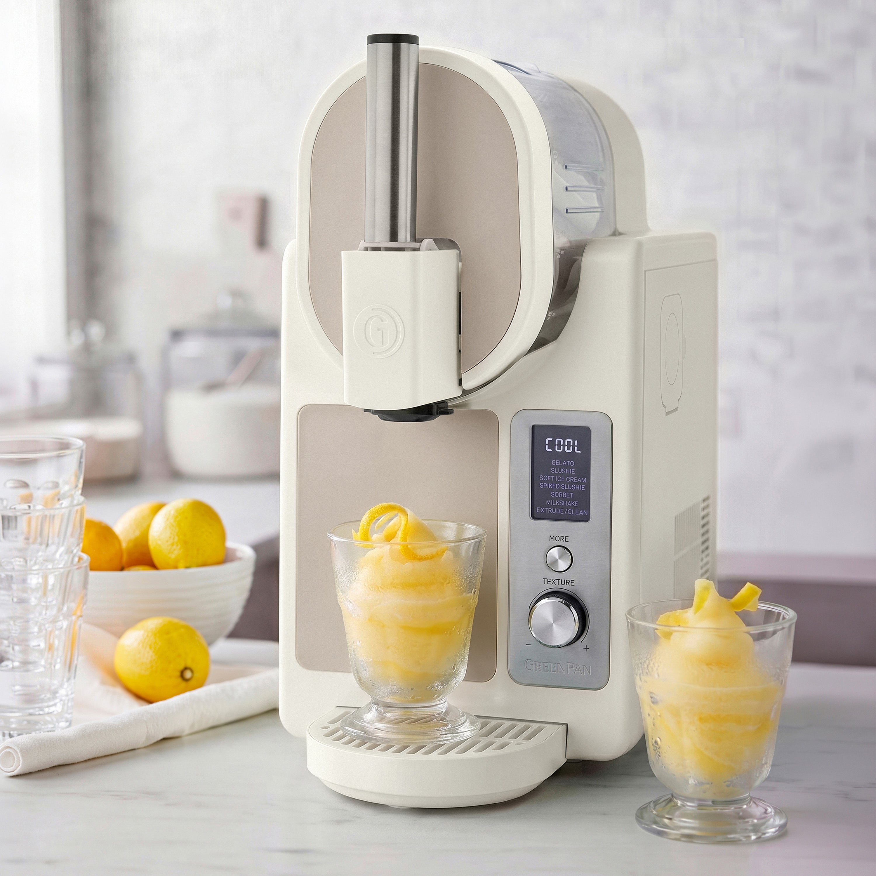 White ice cream maker with two glasses of lemon sorbet on a kitchen counter.