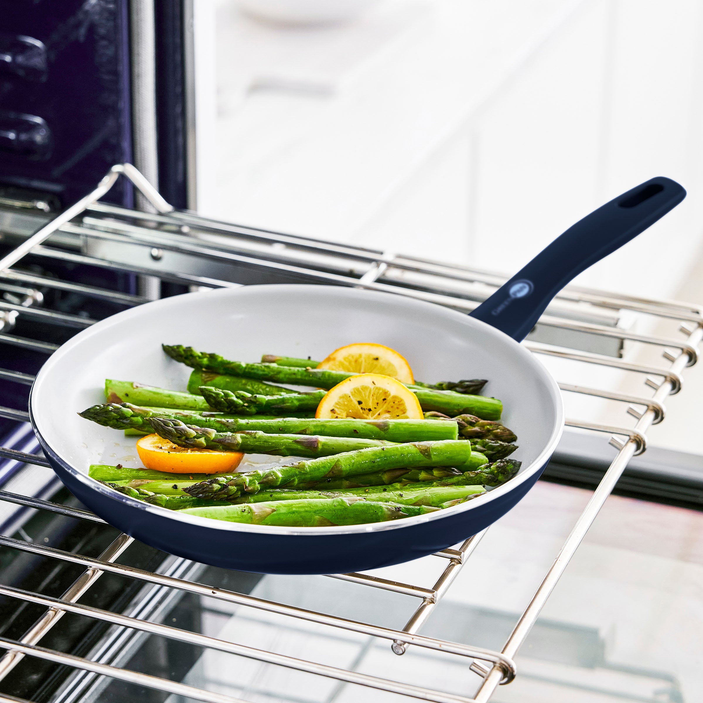 Blue ceramic nonstick pan from 12-piece set with asparagus and lemon on an oven rack.