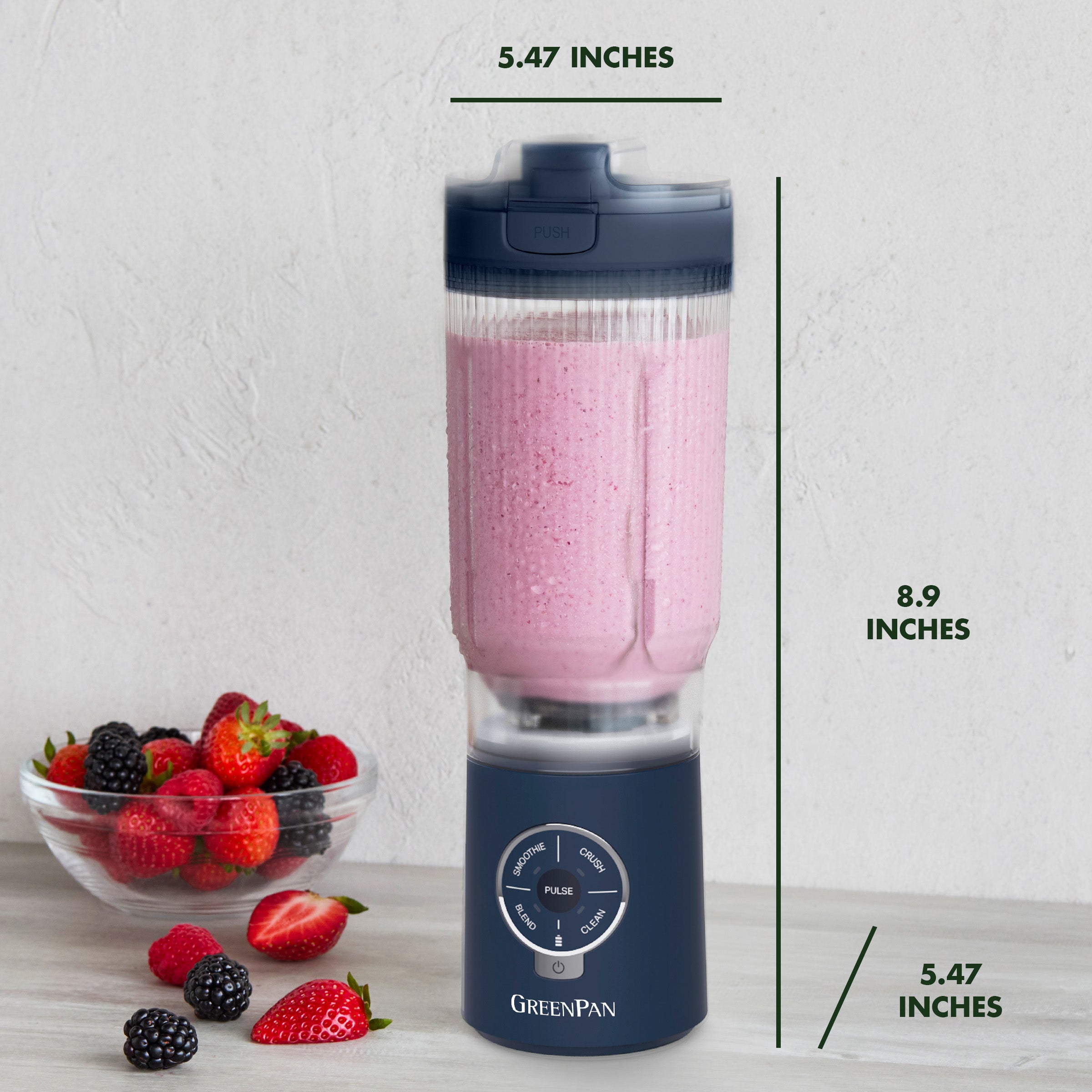 Navy blue portable blender with pink smoothie and a bowl of berries on a light gray background