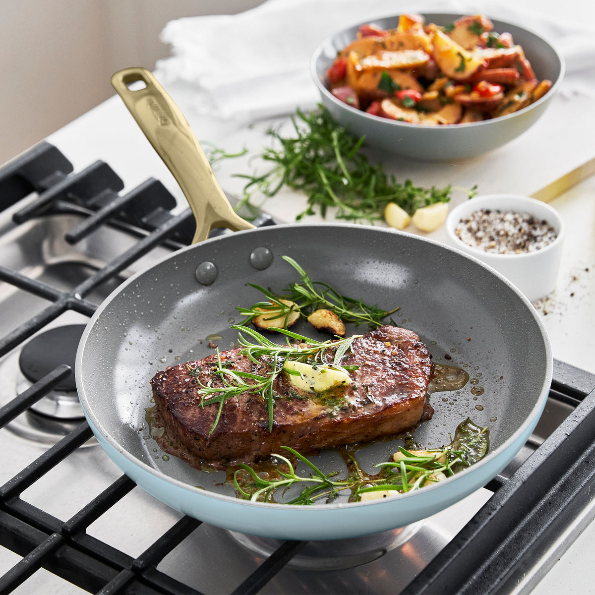 Steak with herbs and vegetables cooks in light blue ceramic nonstick pan from 11-piece set on the stove.