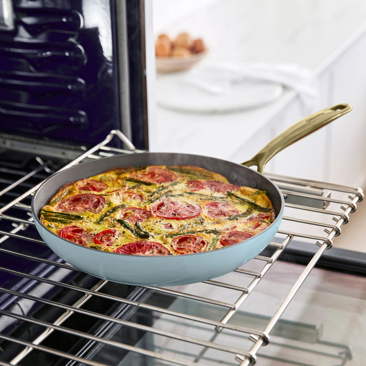 Veggie frittata with tomatoes and greens cooking in a white ceramic nonstick skillet from an 11-piece cookware set on oven rack.