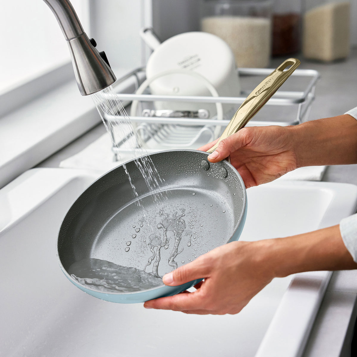 Rinsing a white ceramic nonstick frying pan from an 11-piece cookware set under a kitchen faucet.