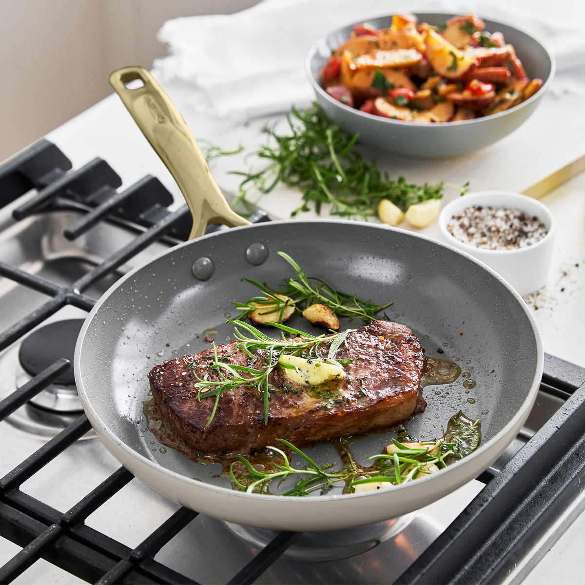 Steak with herbs cooks in Jewel Pro Ceramic Nonstick pan, with bowls of vegetables and spices next to the cookware set.
