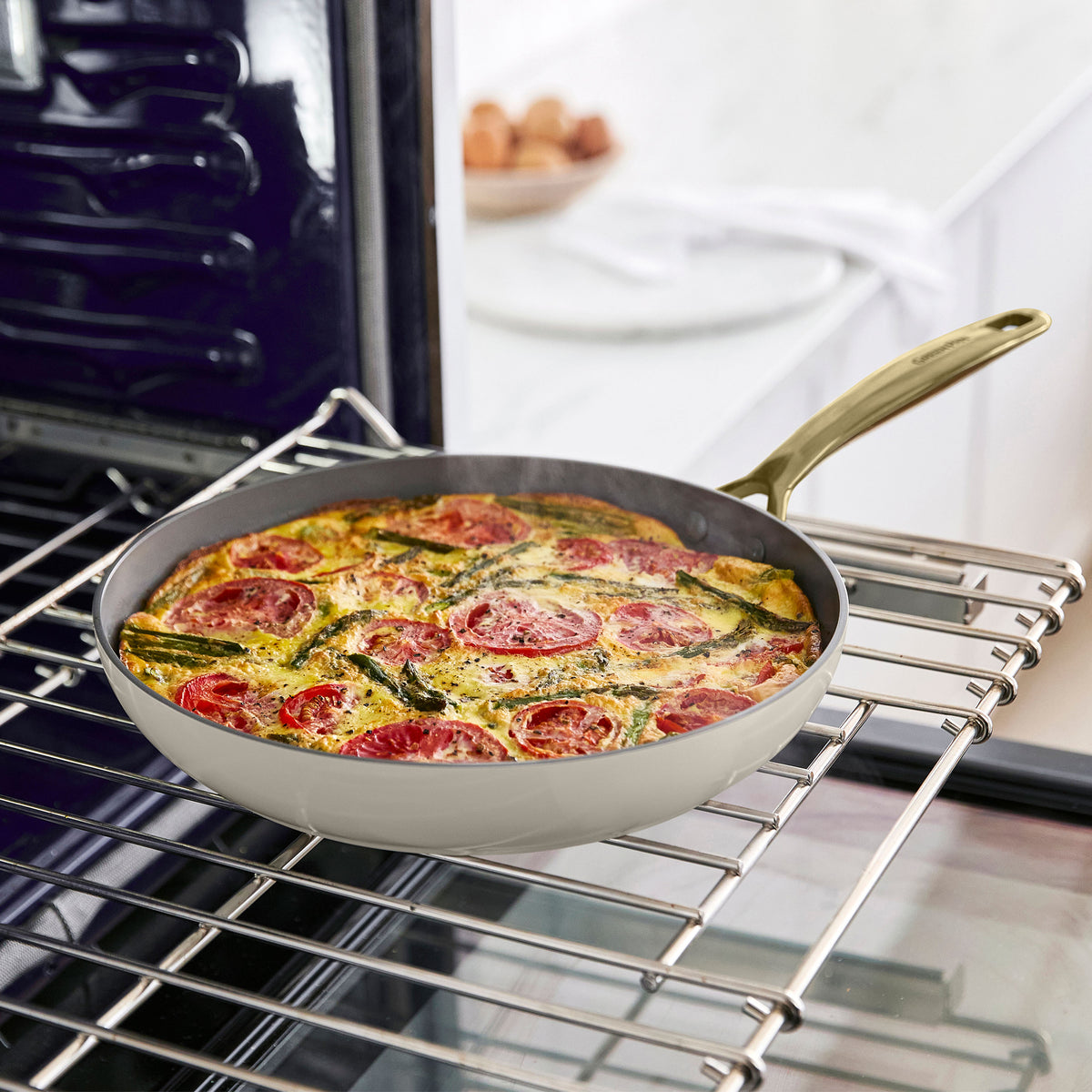 Frittata with tomatoes and greens in a ceramic nonstick skillet on a kitchen counter.