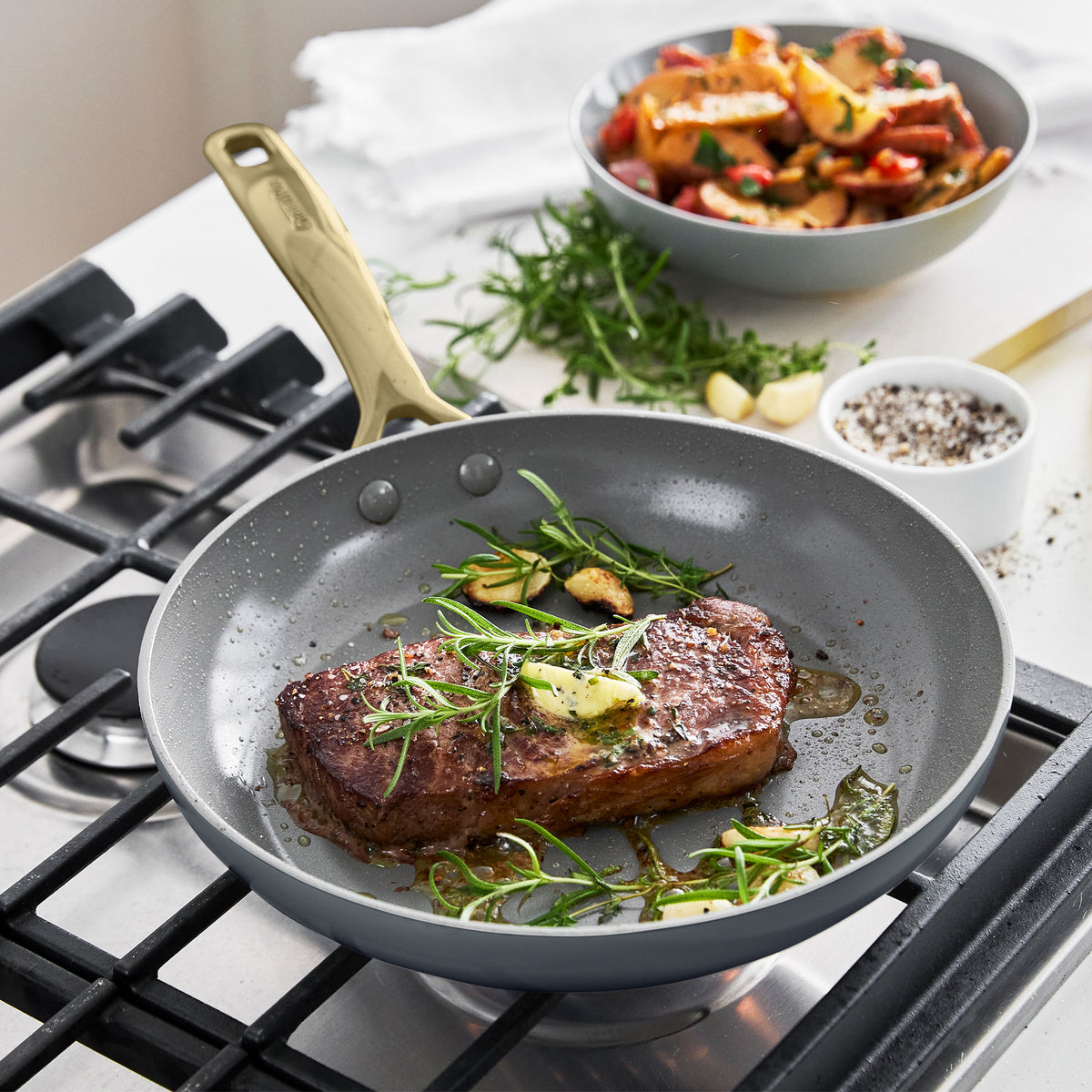 Steak cooking in a ceramic nonstick skillet with roasted vegetables on the side.