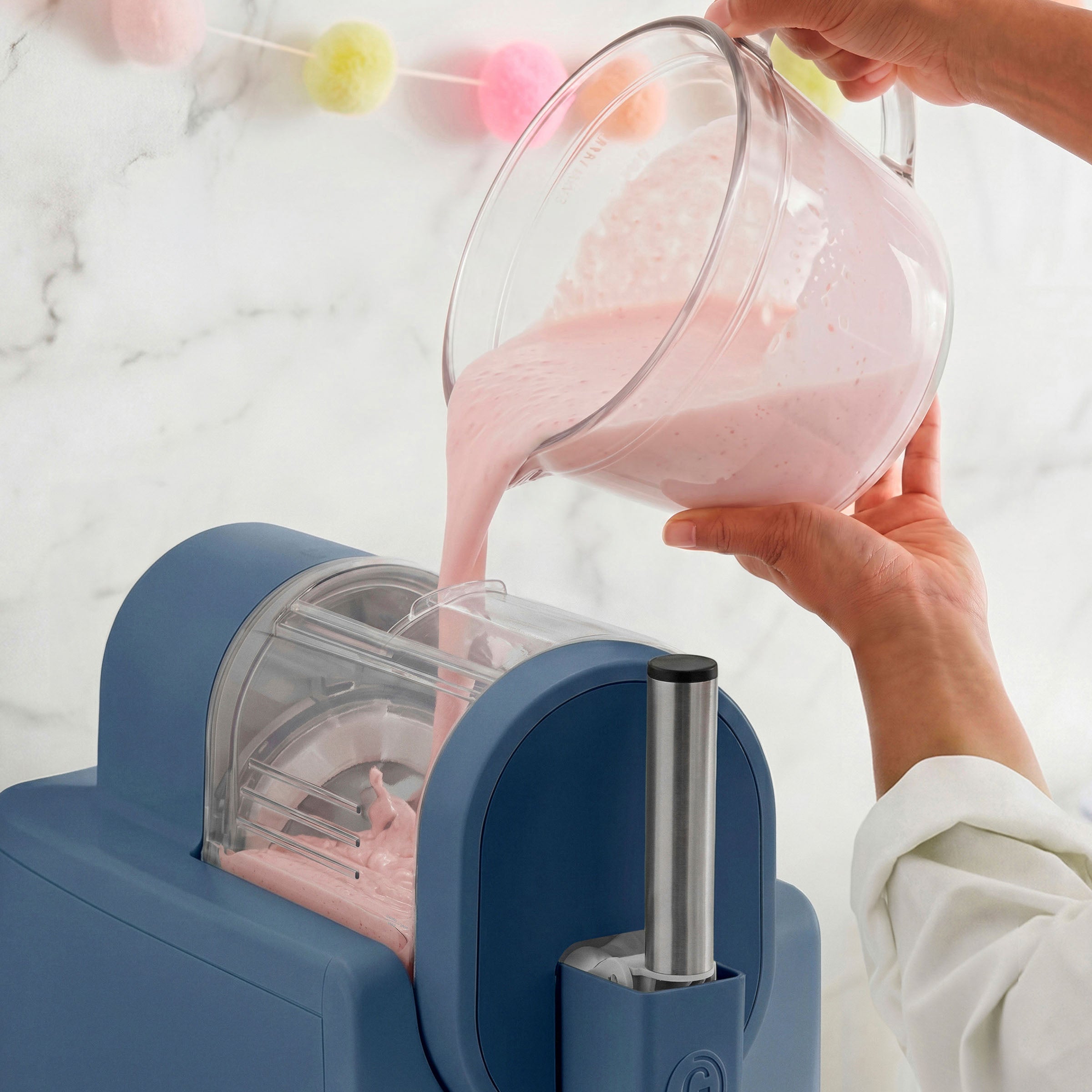 Person pouring pink liquid from a glass pitcher into an ice cream maker
