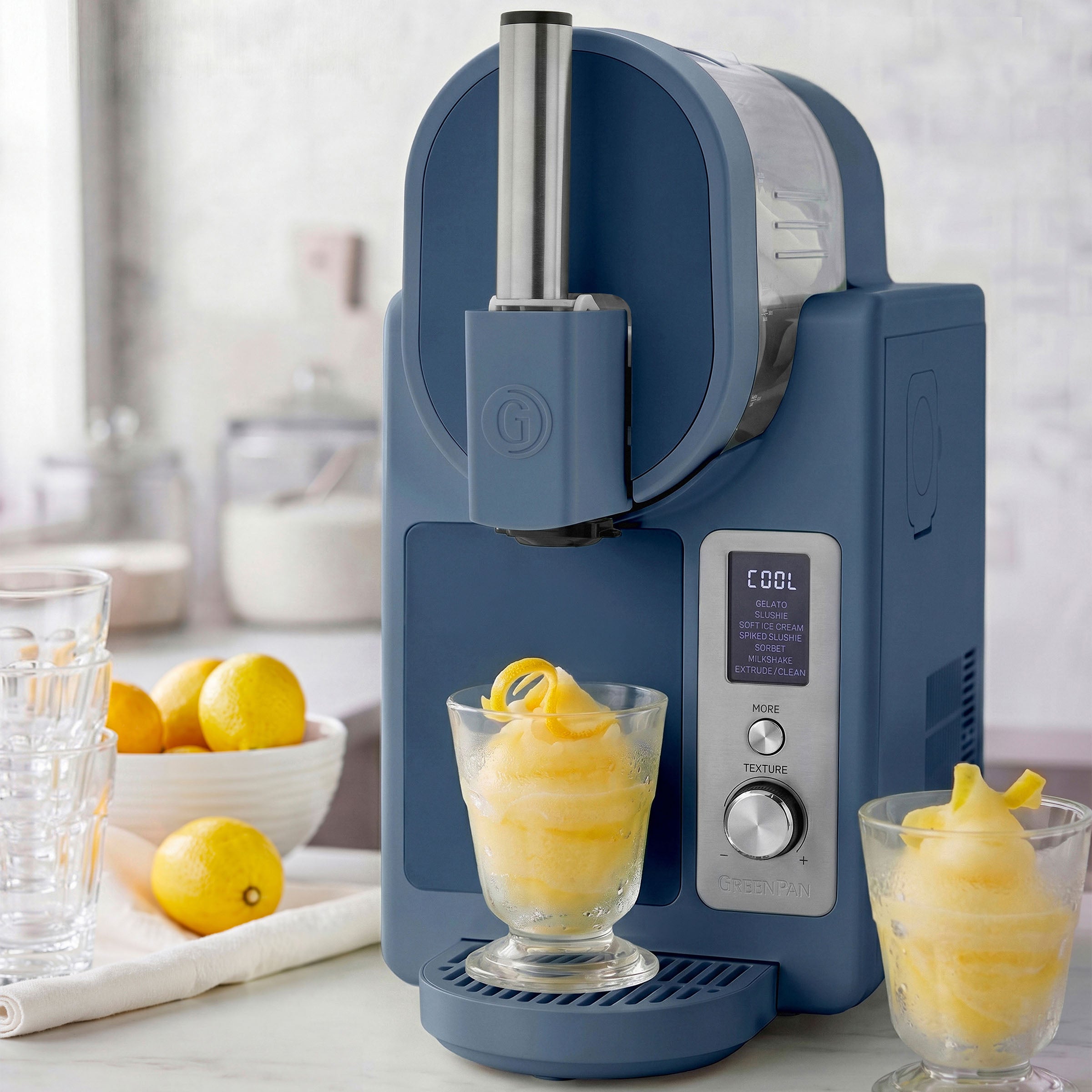 Blue ice cream maker with two glasses of lemon sorbet on a kitchen counter.