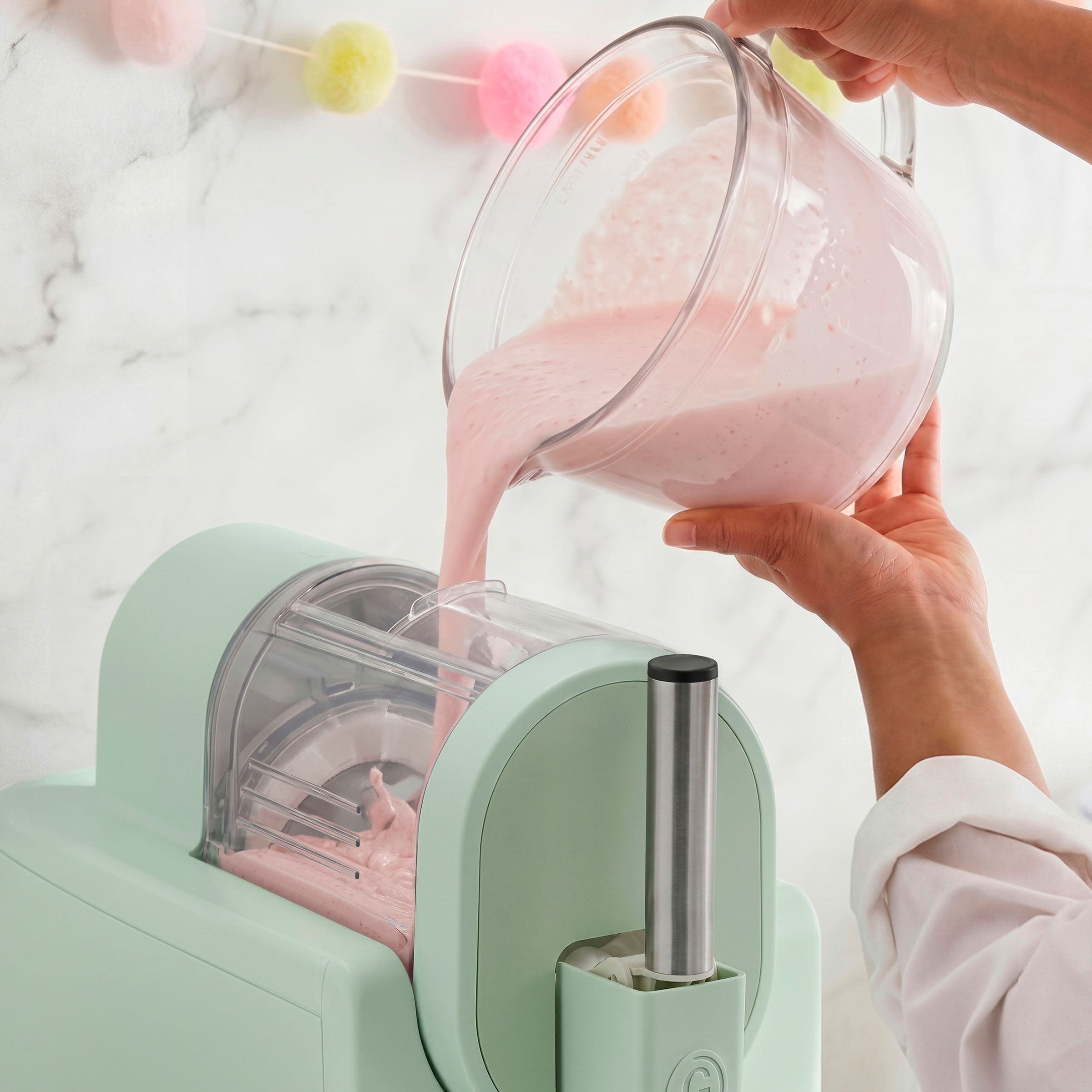 Person pouring pink liquid from a glass pitcher into an ice cream maker
