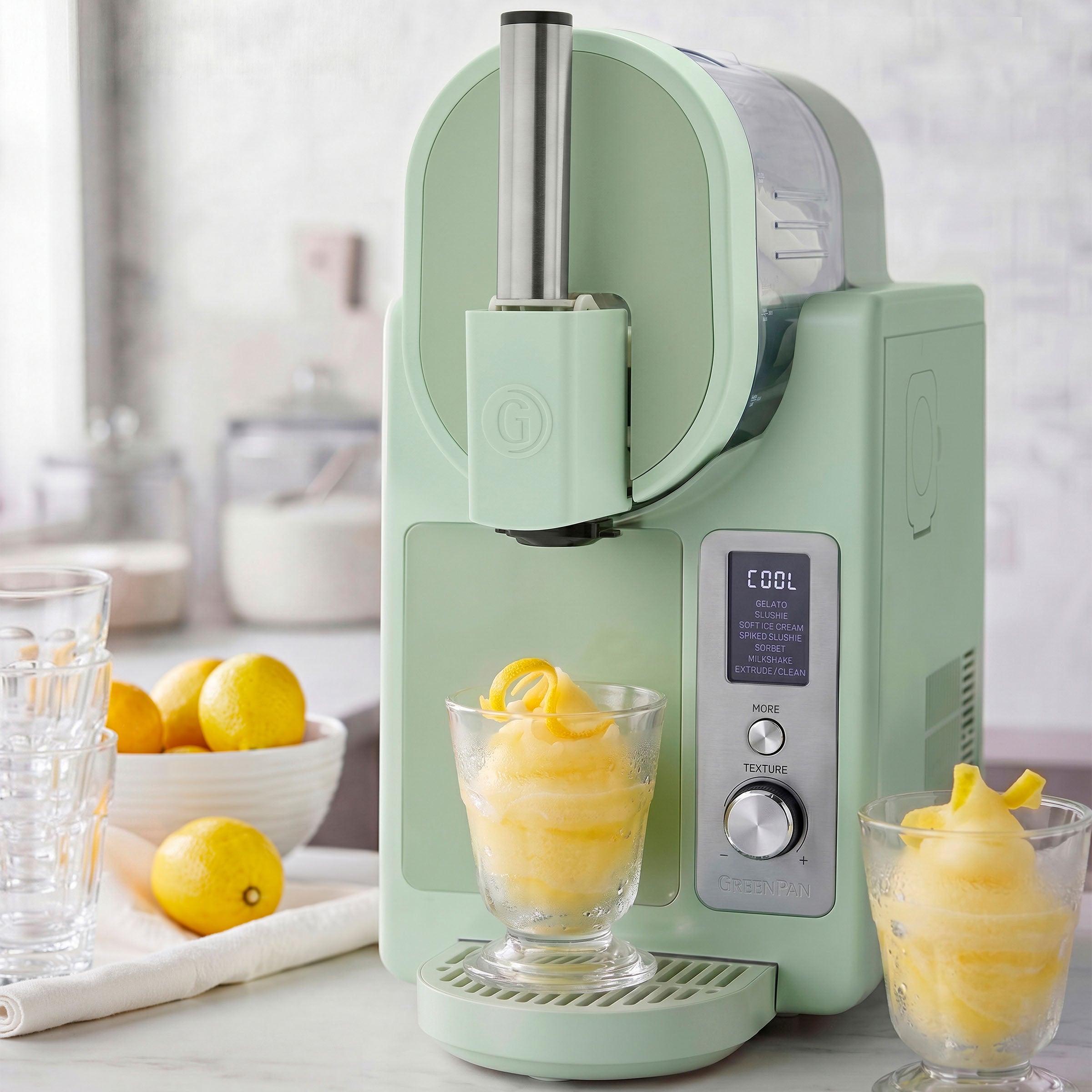 Green ice cream maker with two glasses of lemon sorbet on a kitchen counter.