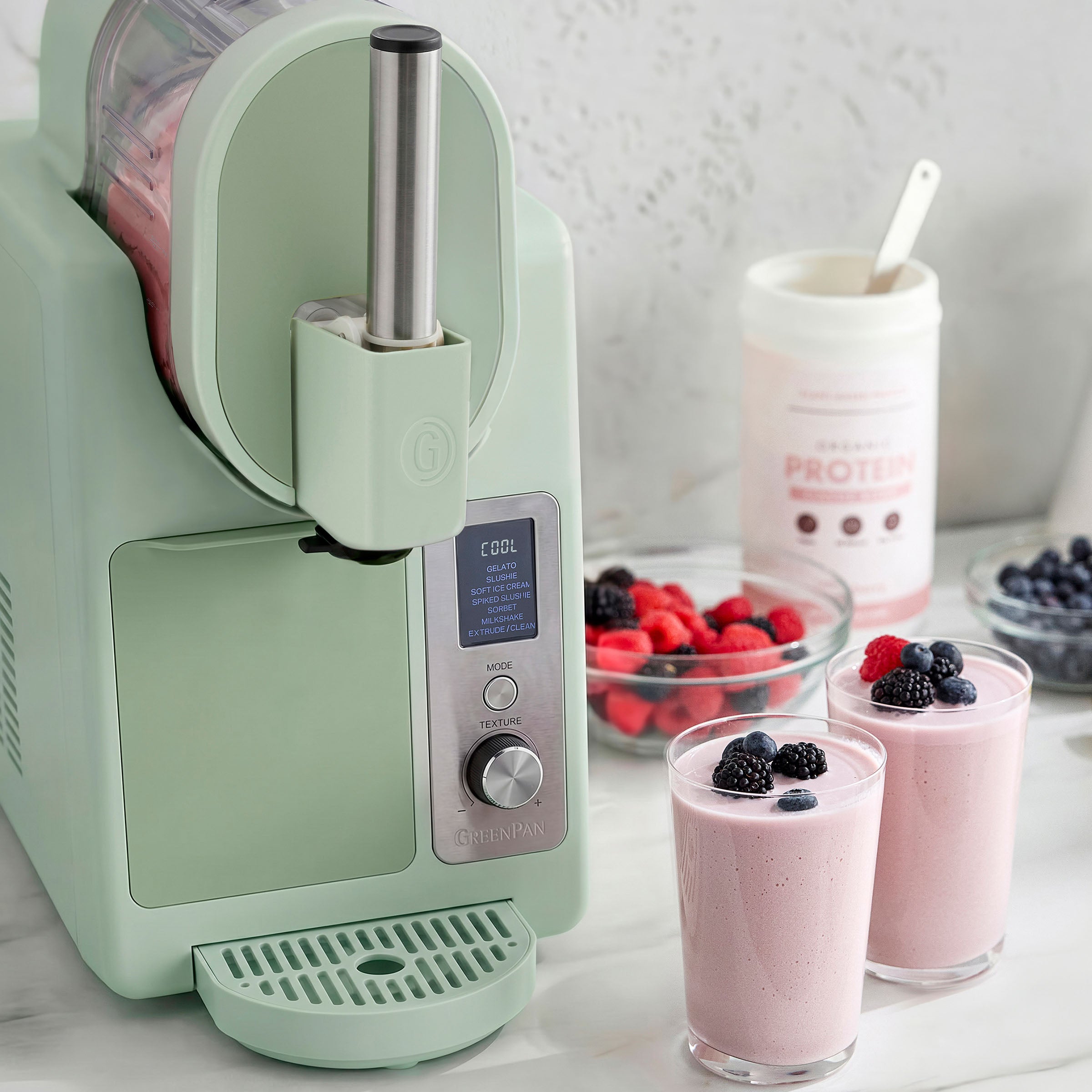 Green ice cream maker with smoothies and berries on a marble countertop