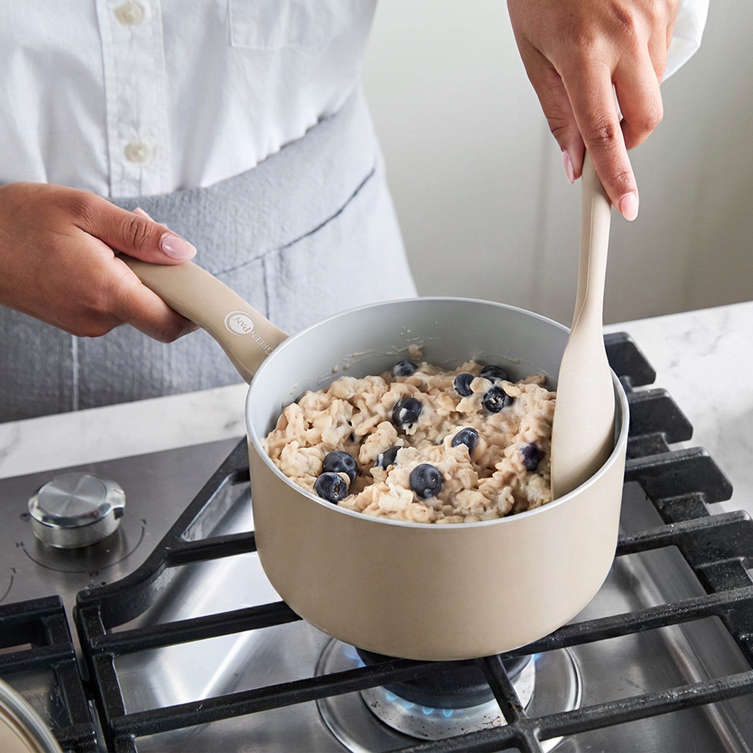 Oatmeal with blueberries cooking in a Dover ceramic saucepan with lid on a stovetop.