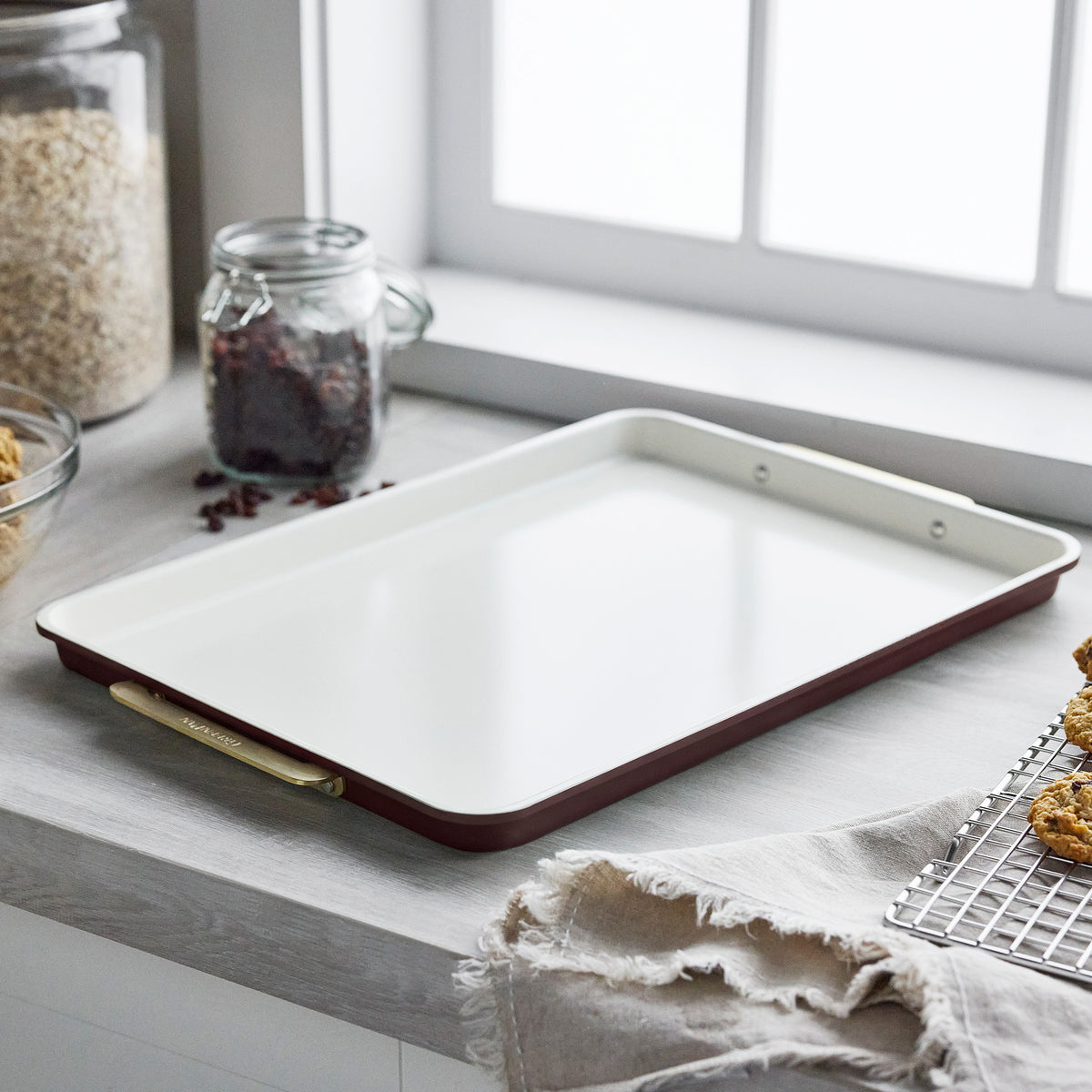 Bordeaux 13″ x 18″ aluminized steel half sheet pan with a white interior and gold handles on a counter.