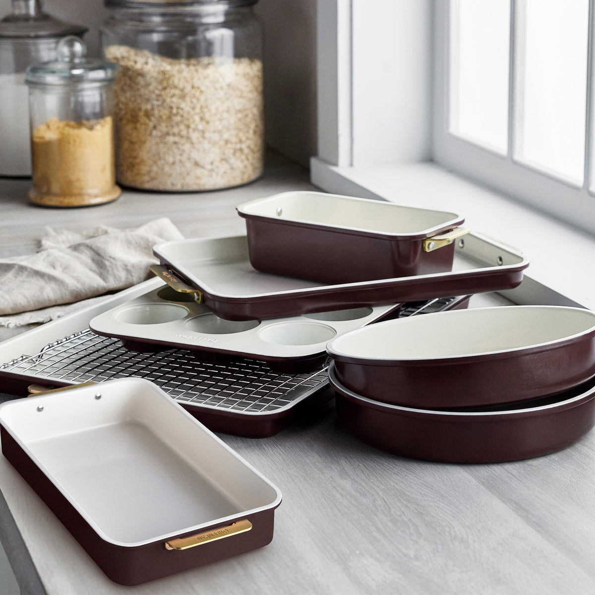 8-piece Reserve bakeware set in bordeaux aluminized steel with cream interiors and gold-tone handles.