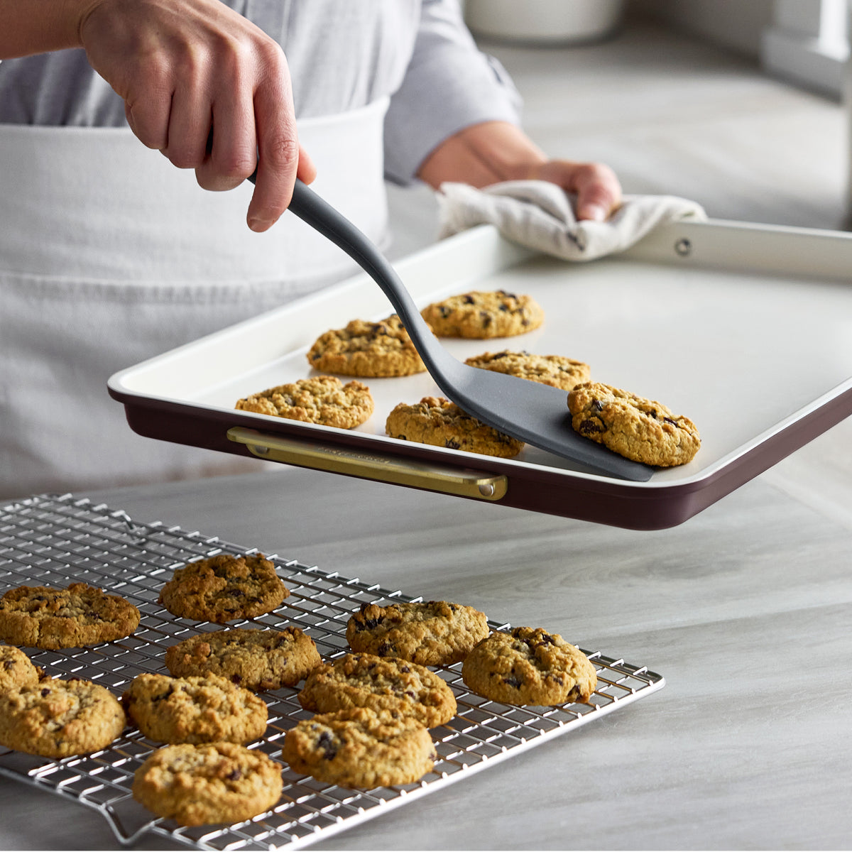 Spatula moving an oatmeal cookie from a Bordeaux Reserve Bakeware 7-piece set baking sheet to a cooling rack.
