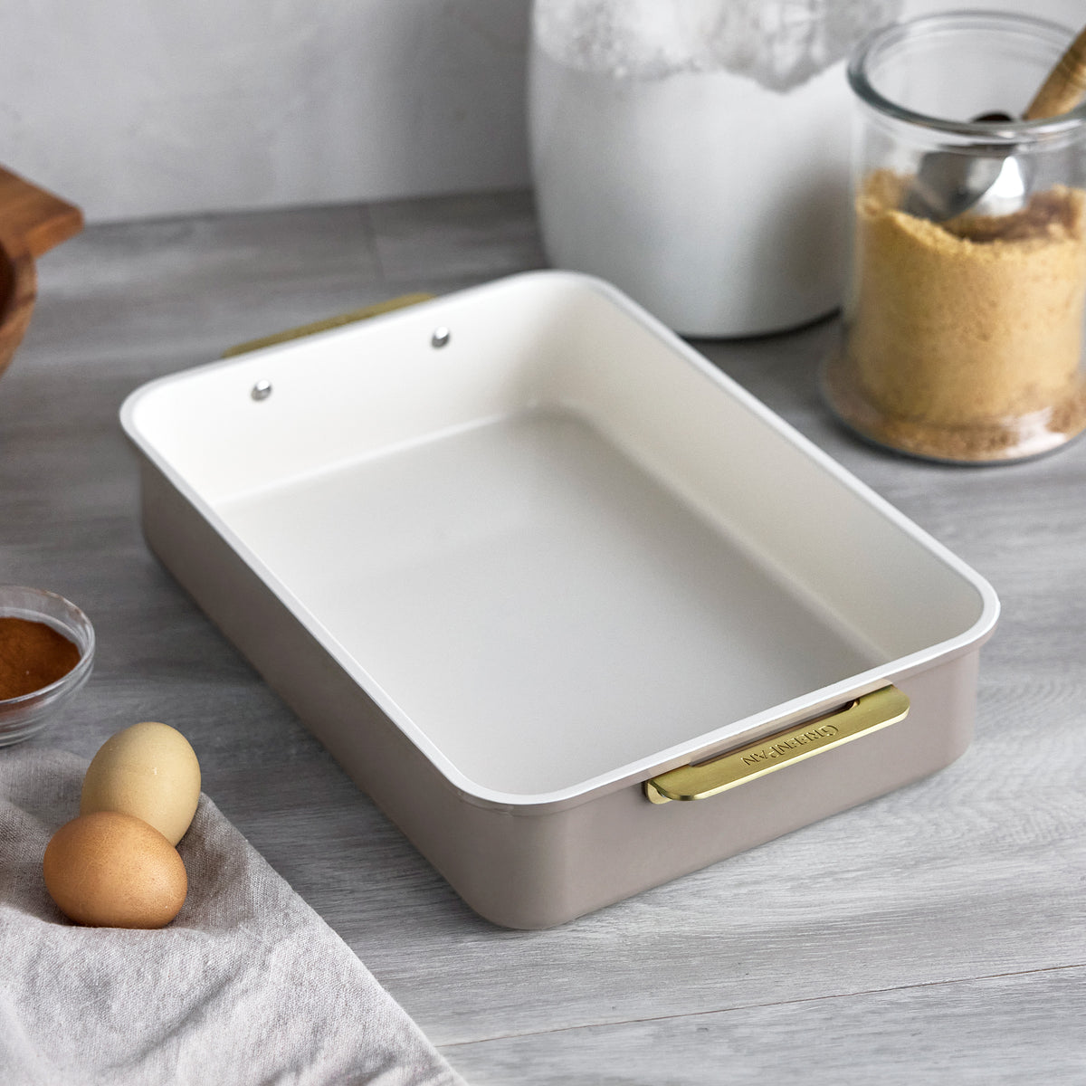 13″ x 9″ rectangular baking pan in latte-colored aluminized steel with a light interior and gold-toned metal handles.