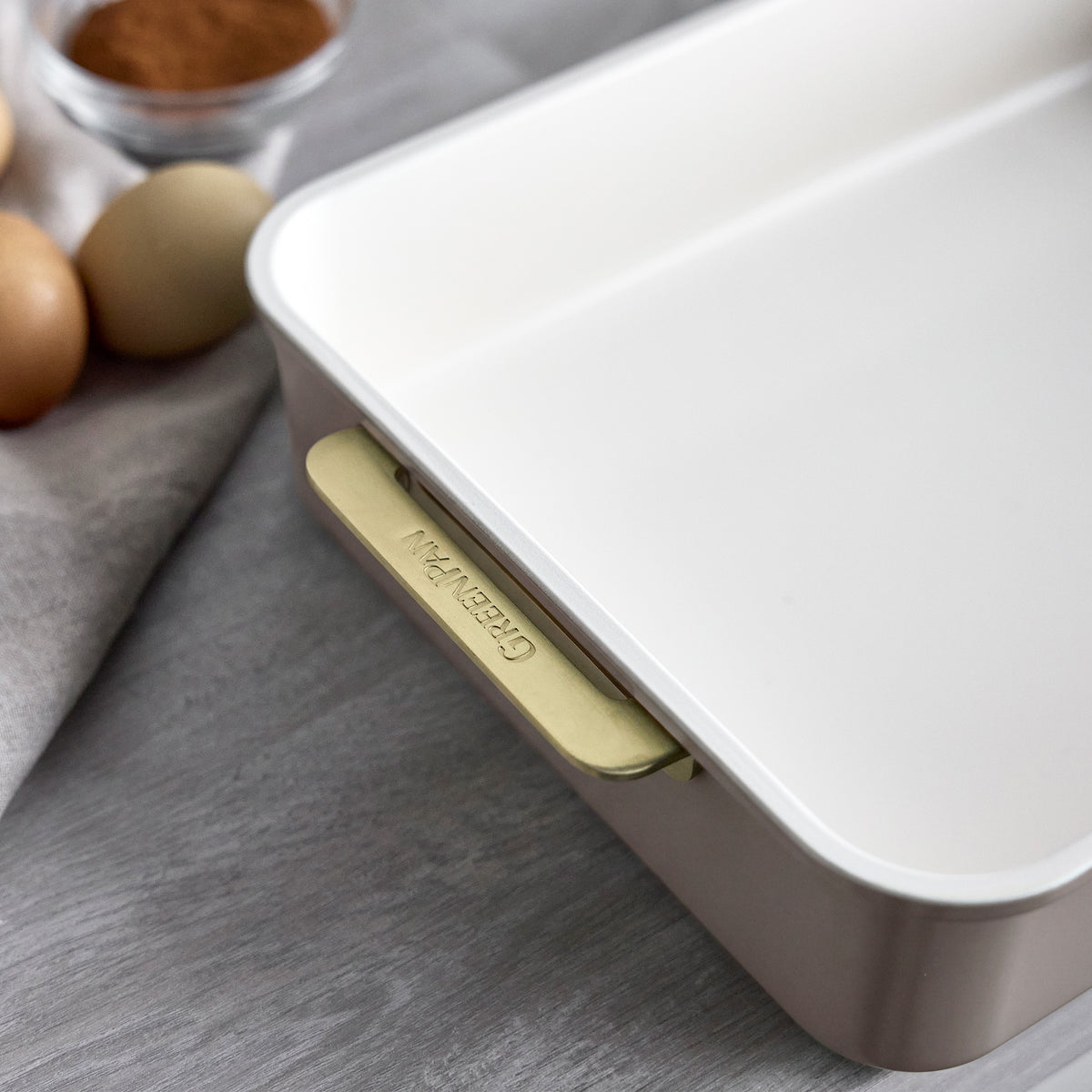 Latte 13″ x 9″ rectangular baking pan with a white nonstick interior and gold-toned handles.