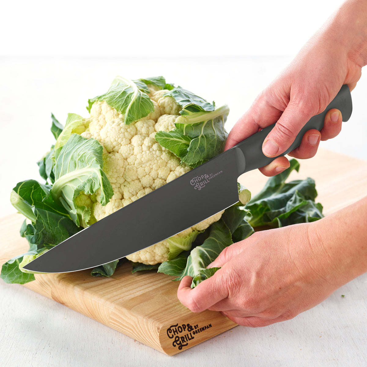 Chop  Grill 2-piece knife set slicing cauliflower on a wooden board, surrounded by leafy greens.