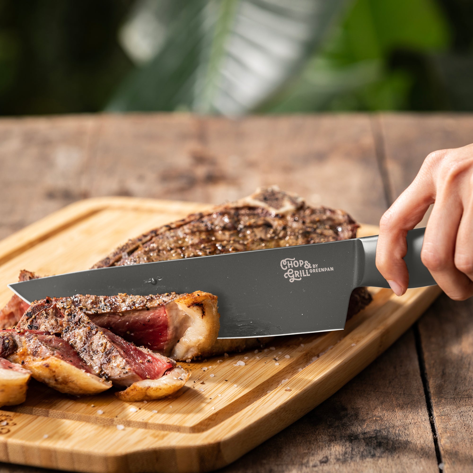 Person cutting a steak on a wooden board with a knife, outdoor setting