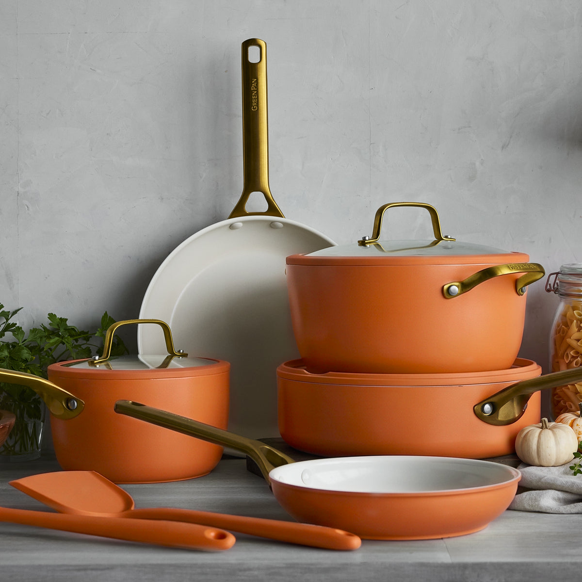 Stackable 10-piece cookware set in orange and white with gold handles, includes pots, pans, and utensils. Ceramic finish.