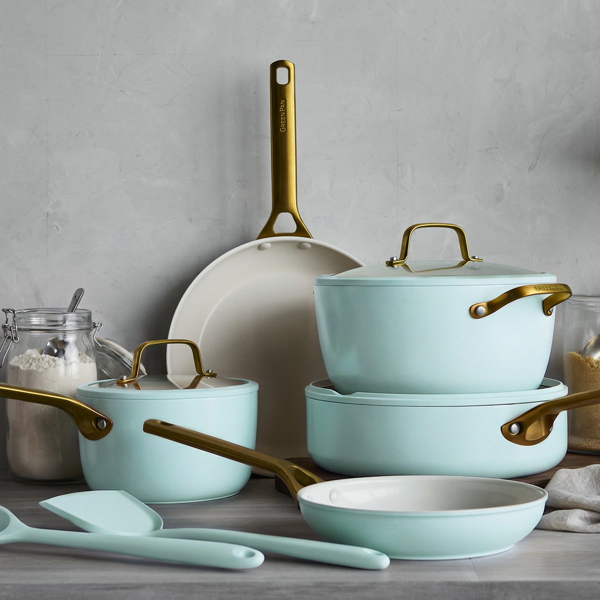 Blue ceramic nonstick cookware set with gold handles on a gray counter, near clear flour and sugar jars, 10 pieces visible.