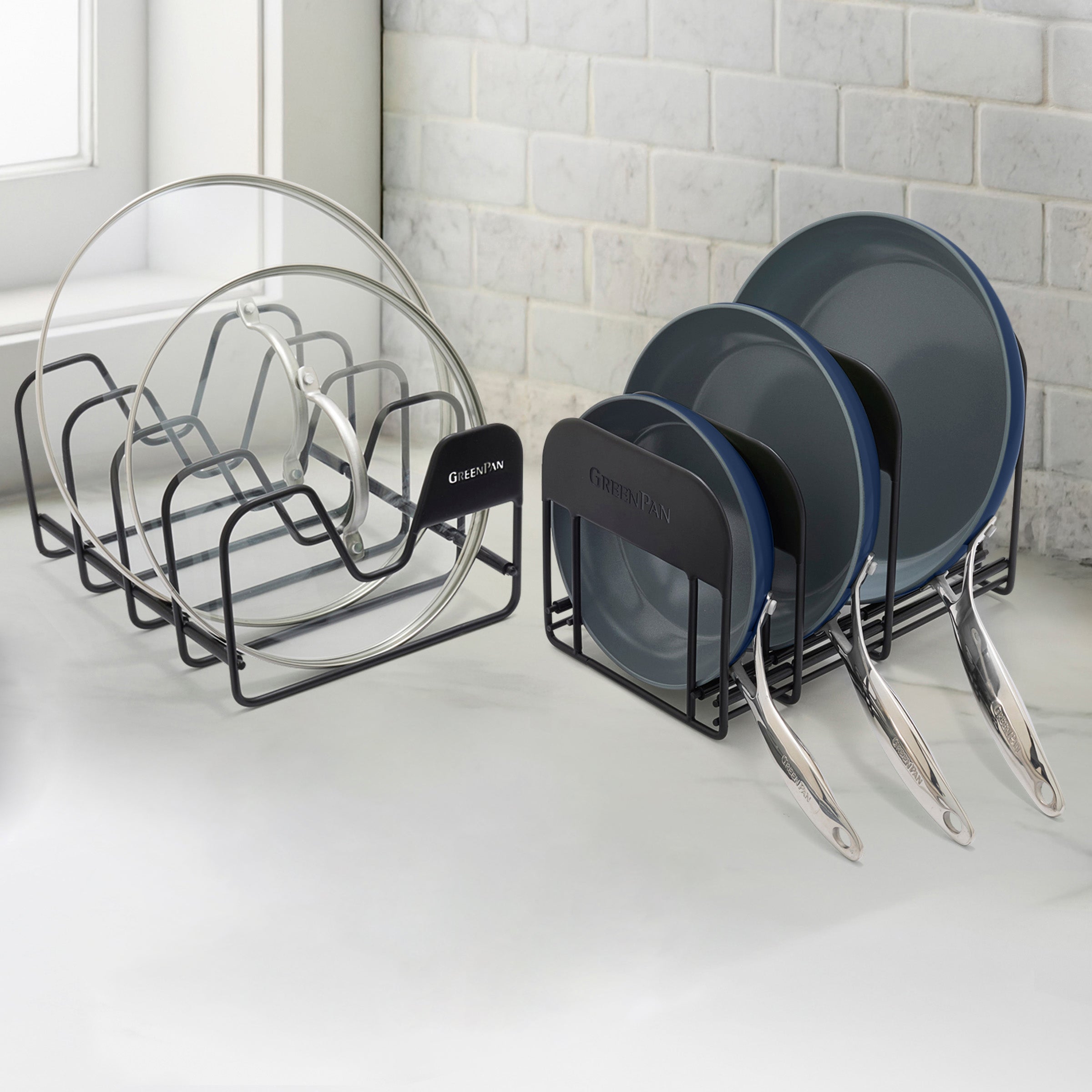 Two sets of twilight blue nonstick frypans sit on a white kitchen counter with a tiled backsplash in the background.