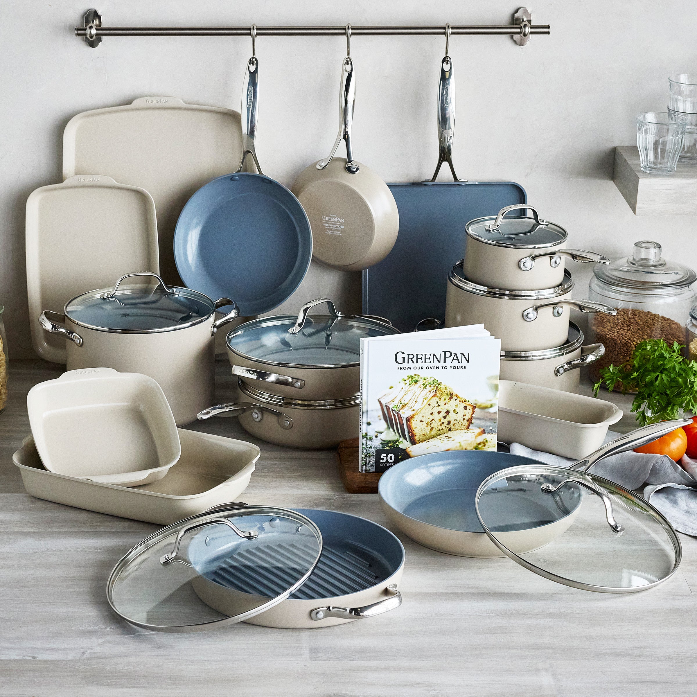 24-piece taupe ovenware set with glass lids arranged on a kitchen counter beside fresh produce.