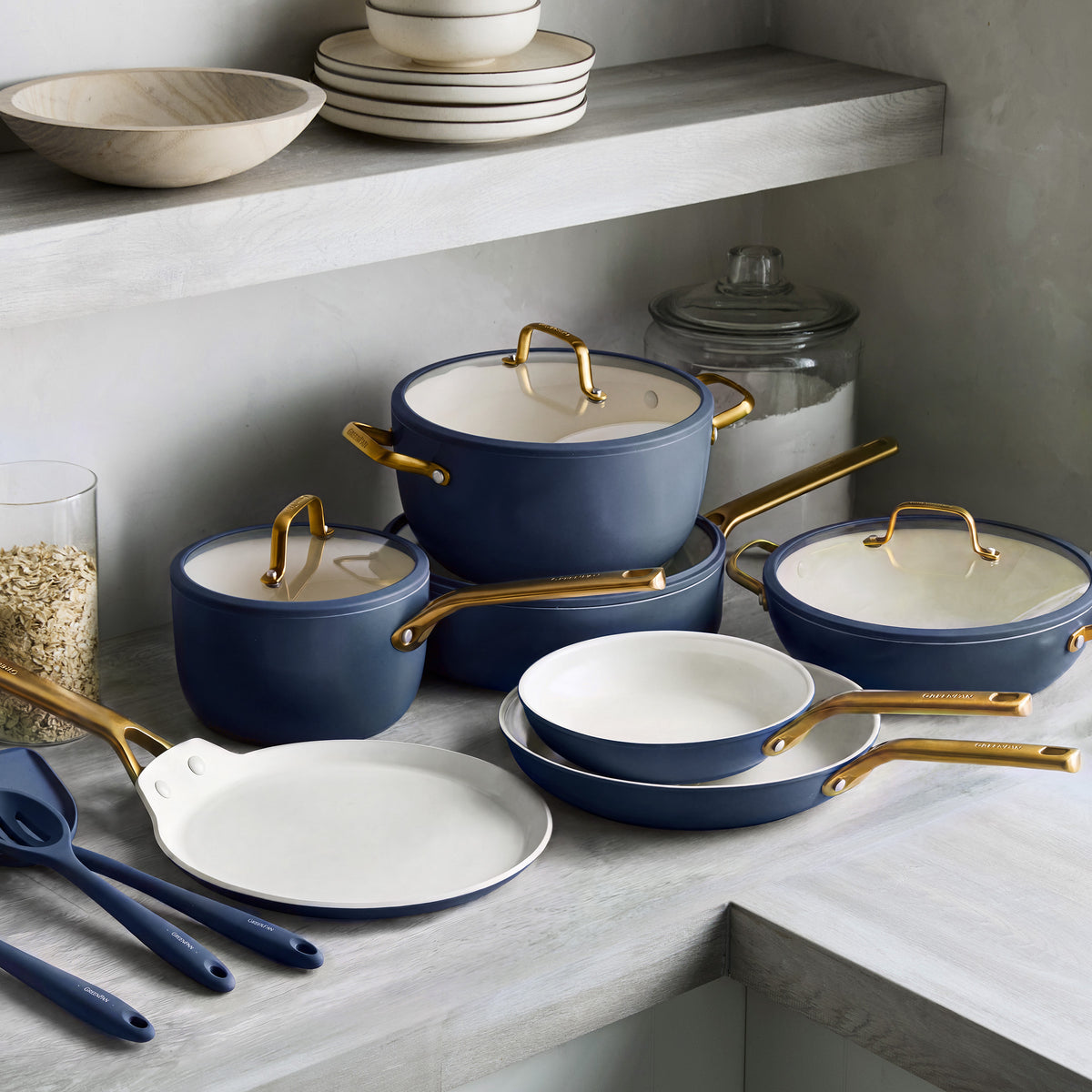14-piece ceramic nonstick cookware set in twilight blue with gold handles displayed on a grey counter among kitchen items.