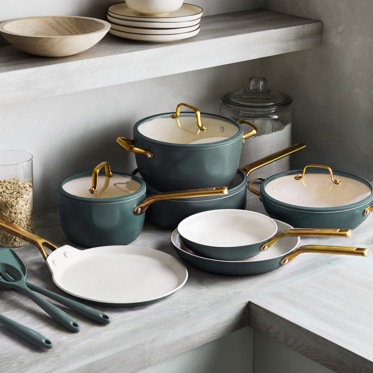 14-piece spruce ceramic cookware set with gold handles on a counter, including various pans and utensils.