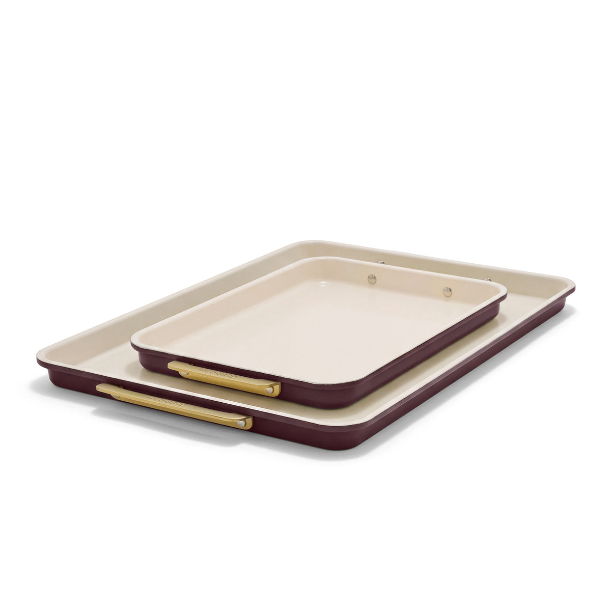 Two rectangular burgundy Reserve Bakeware sheet pans with cream interiors and gold-toned handles.